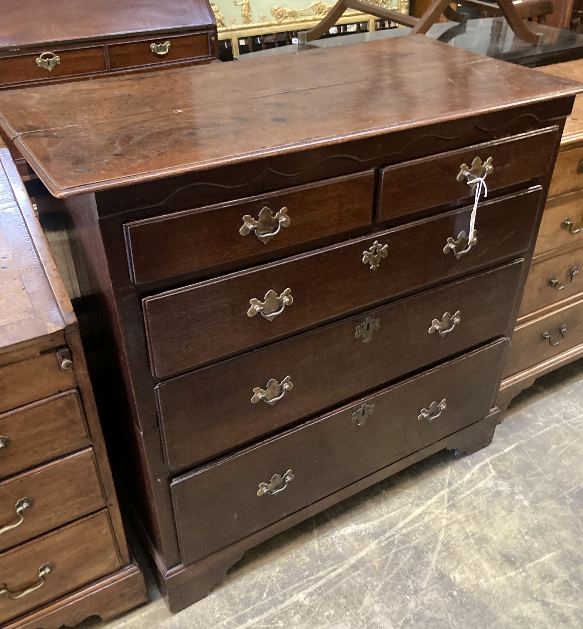 A George II provincial oak chest of two short and three long drawers, with brass drop handles and ogee arched frieze, on bracket feet,